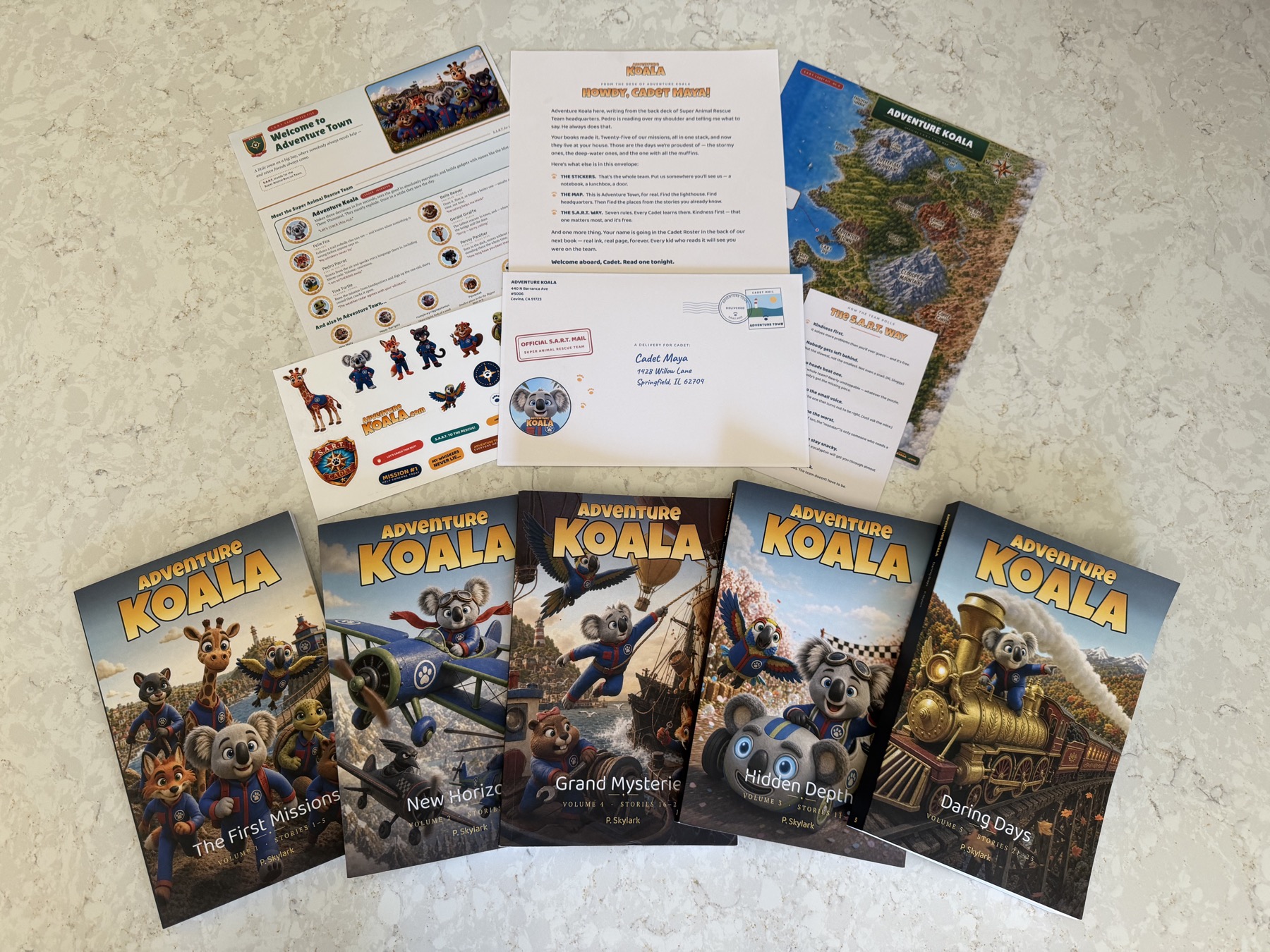 Everything in the box: all five Adventure Koala books fanned out below the full Cadet Welcome Kit — the letter, the Adventure Town map, the Cadet Field File, the sticker sheet, the stamped envelope, and The S.A.R.T. Way card